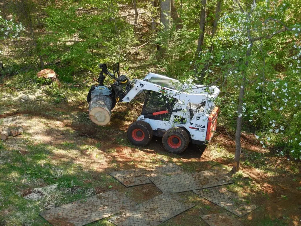 Skid steer moving a log round over ground-protection mats