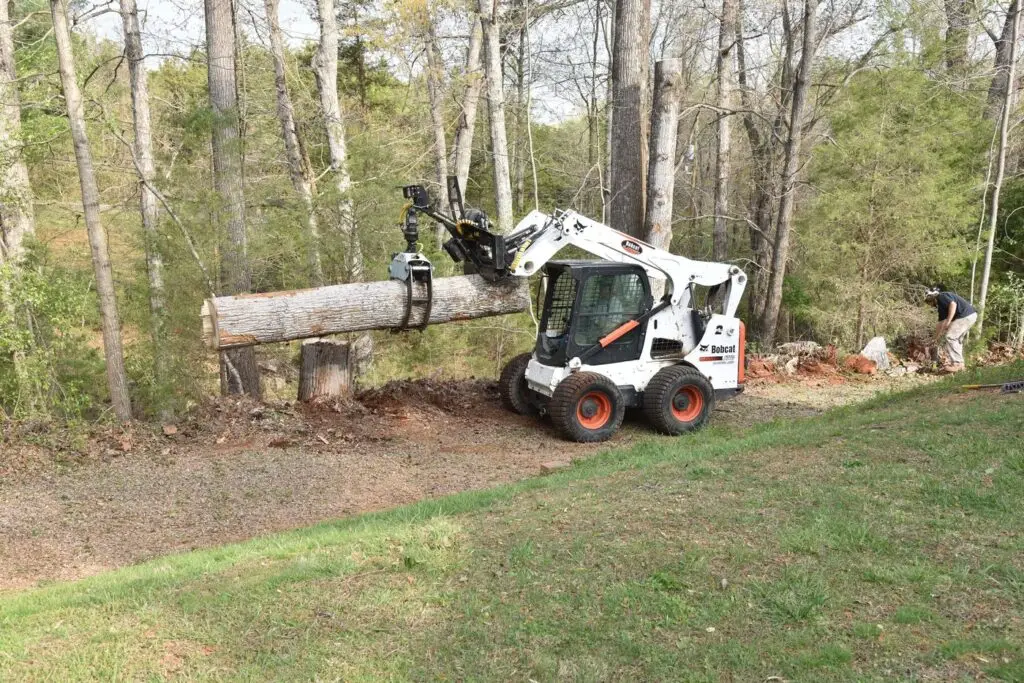 Skid steer carrying a log off a wooded lot