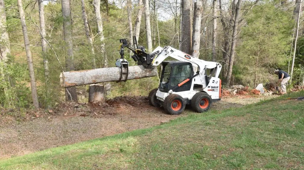 Skid steer carrying a log across a yard