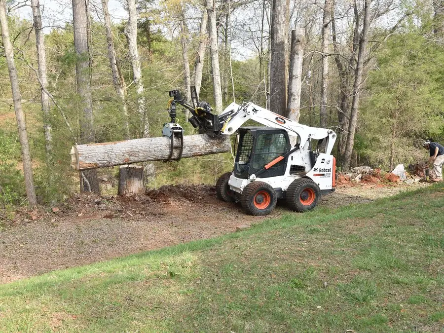 Skid steer carrying a log across a yard