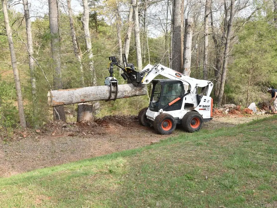 Skid steer carrying a log off a wooded lot
